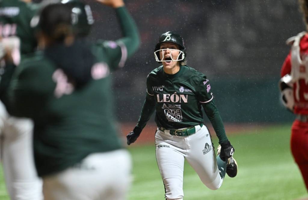 A player in a green baseball uniform celebrating enthusiastically as she runs towards her teammates amid a rainy game.