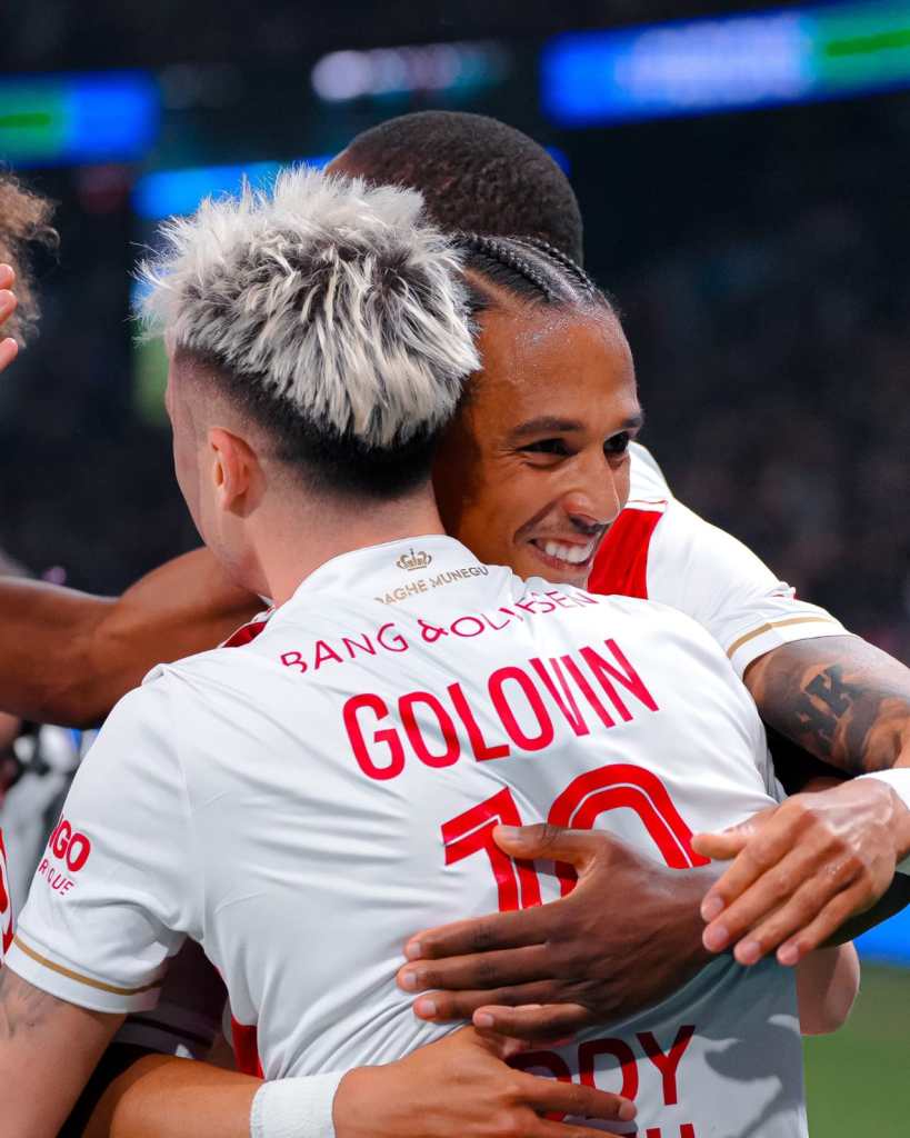 A group of football players celebrating a goal, embracing each other in a moment of joy.